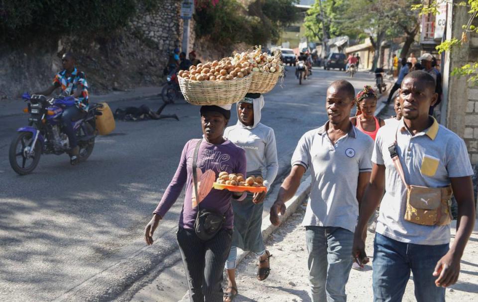 Motorcyclists navigate around a charred body lying in the road as pedestrians walk past, in the Petion-Ville neighborhood of Port-au-Prince, Haiti, Wednesday, March 20, 2024.