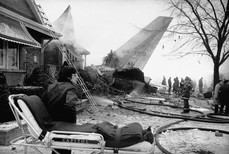 A person stands by a stretcher ready for victims of a United Air Lines plane that crashed on Chicago's southwest side, Dec. 8, 1972. Firemen stand on the wreckage of the plane and spray water on a house set on fire in the crash. (AP Photo/Charles E. Knoblock)