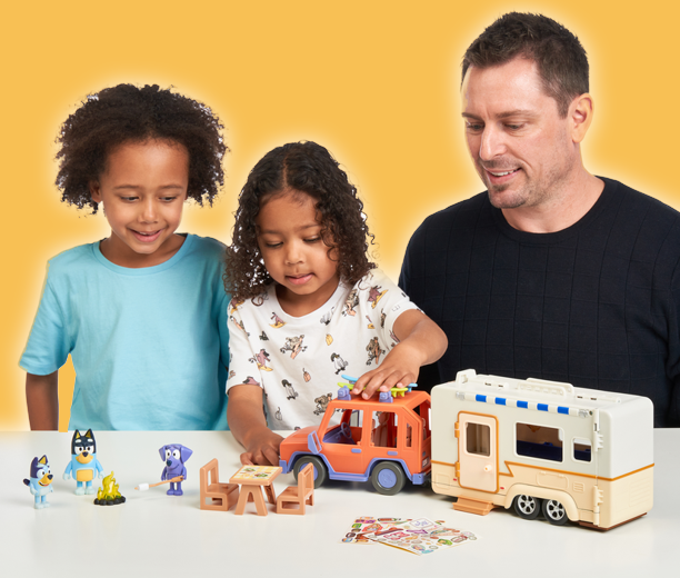 A man and two children playing with the Bluey Camper playset.