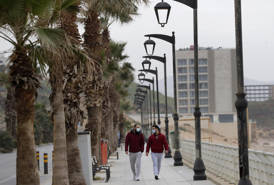 People wearing masks to help prevent the spread of the coronavirus walk on a waterfront promenade along the Mediterranean Sea, along the Ramlet al-Baida public beach, in Beirut, Lebanon, Wednesday, Jan. 27, 2021. Lebanon, a country of nearly 5 million and over 1 million refugees, is going through an unprecedented economic crisis that preceded the pandemic and restrictions imposed to combat it. (AP Photo/Hussein Malla)