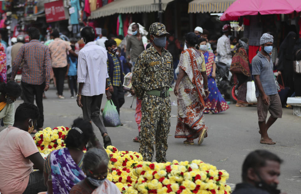 An Indian municipal officer, center, stands to ensure people follow COVID-19 guidelines at a busy market in Bengaluru, India, Tuesday, Jan. 5, 2021. India authorized two COVID-19 vaccines on Sunday, paving the way for a huge inoculation program to stem the coronavirus pandemic in the world's second most populous country. (AP Photo/Aijaz Rahi)