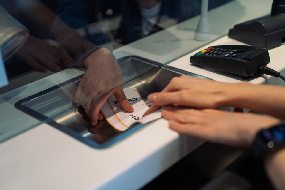 Person at a counter receiving a ticket from an attendant through a slot