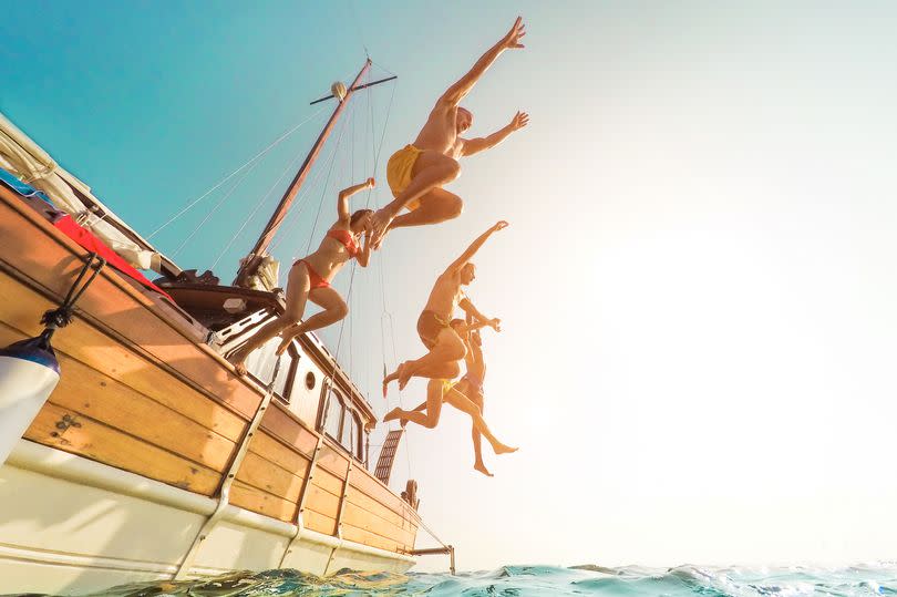 Young people jumping inside ocean in summer excursion day - Happy friends diving from sailing boat into the sea - Vacation, youth and fun concept - Focus on bodies silhouette - Fisheye lens distortion