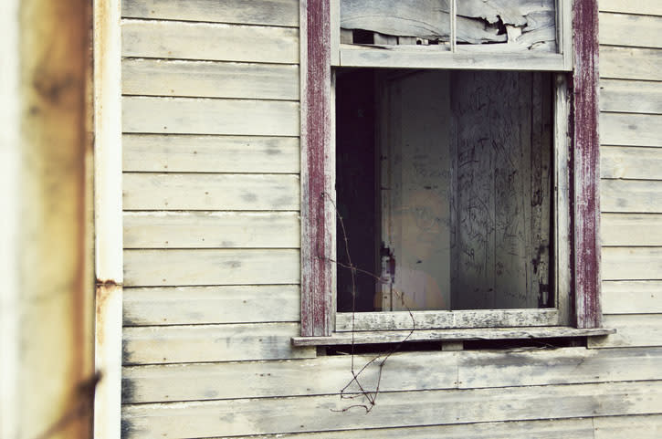 An old, weathered wooden house with a broken window and graffiti inside