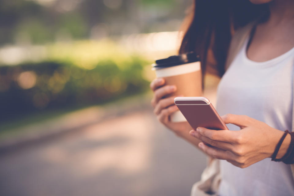 A woman looking at her smartphone while drinking coffee