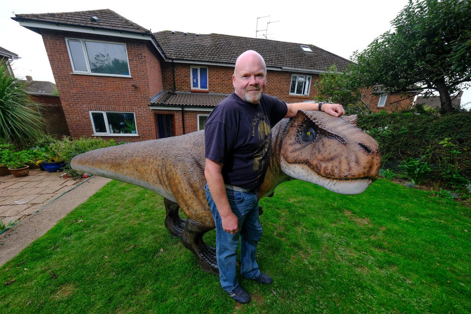 A wacky husband shocked his wife who wanted to brighten up their garden with a gnome - by installing a 12ft-tall replica of a T-REX on the patio. Adrian Shaw, 52, snapped up the 14-stone resin and fiberglass dinosaur and hired a crane to winch it into position on Thursday (3/9). He came up with the madcap-scheme after wife Deborah, 53, begged him to clean up the back garden of their home in Leamington Spa, Warks. The IT analyst paid £1,600 for the replica of the terrifying beast, which he named ‘Dave’ and put it on the patio.