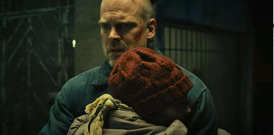 joyce byers hugging hopperin a russian prison, with her back to the camera. hopper has a bewildered, almost overwhelmed expression on his face