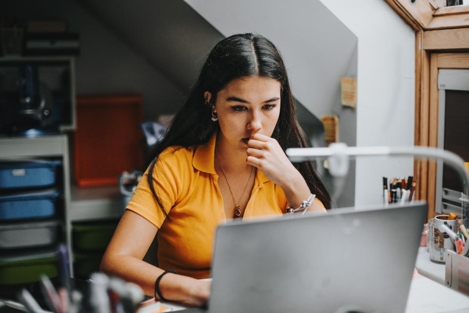 hispanic latina college student works on assignment in her dorm room.She is smiling and in the background there is a big blackboard