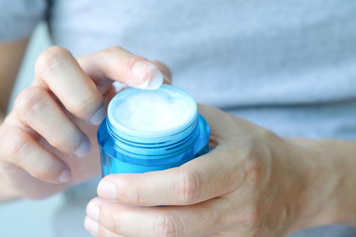 Hand of woman holding moisturizer cream and serum. She applying a facial cream