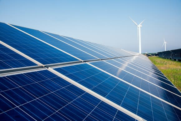 Large ground-mounted solar array with a wind turbine in the background.