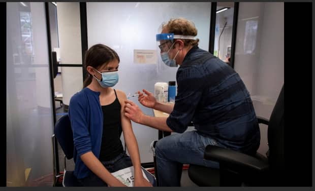 Julia Lorenti, 13, gets a dose of the Pfizer-BioNTech COVID-19 vaccine from Dr. Gary Bloch at a clinic for people with Indigenous ancestry in Toronto on May 25. Canada has become a world leader when it comes to share of population with at least one dose of the COVID-19 vaccine. (Evan Mitsui/CBC - image credit)