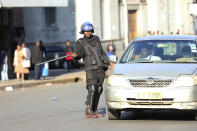 A riot police gives direction to a driver in Harare, Friday, Aug. 16, 2019. Zimbabwe's police patrolled the streets of the capital Friday morning while many residents stayed home fearing violence from an anti-government demonstration planned by the opposition. (AP Photo/Tsvangirayi Mukwazhi)