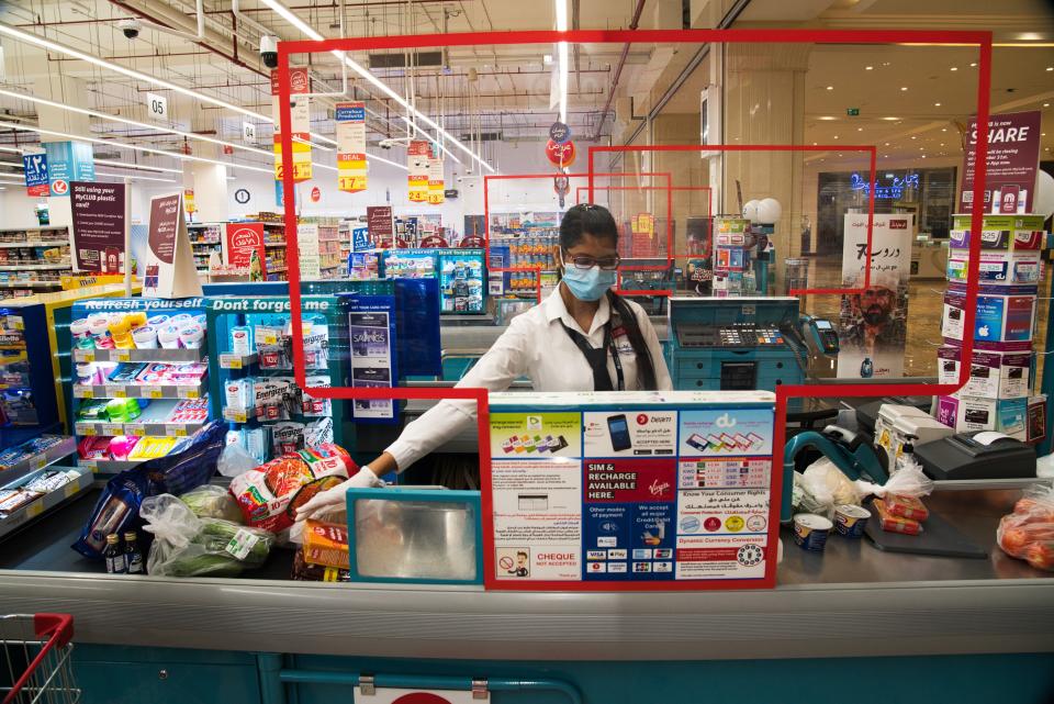 In this April 19, 2020 photo, cashier Valancy Fernandes of India, wearing a surgical mask and gloves to help prevent the spread of coronavirus, works at a Carrefour supermarket in Dubai, United Arab Emirates. Frontline workers across Arab Gulf countries are uniquely almost entirely foreigners. They risk exposure to the novel coronavirus, ensuring patients are cared for, streets are sanitized, packages are delivered and grocery stores are stocked. The global pandemic has drawn attention to just how vital foreigners are to the Arab Gulf countries where they work. (AP Photo/Jon Gambrell)