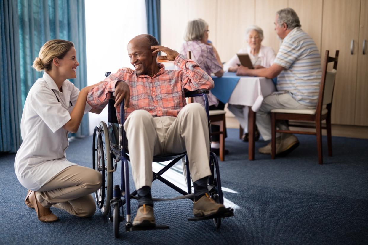 nursing home caregiver checking on elderly resident in wheelchair