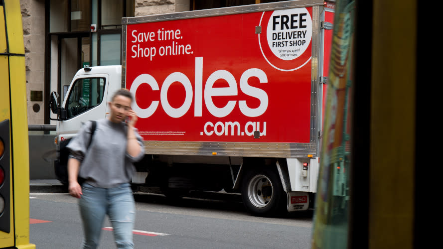 A woman walking by a Coles van on the street.