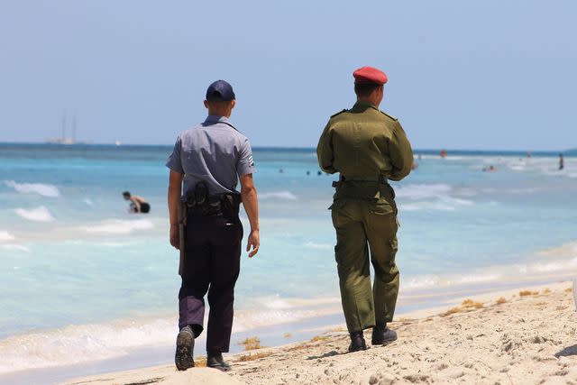 <p>Getty Images</p> A Cuban soldier and a Cuban police officer walk along a beach together