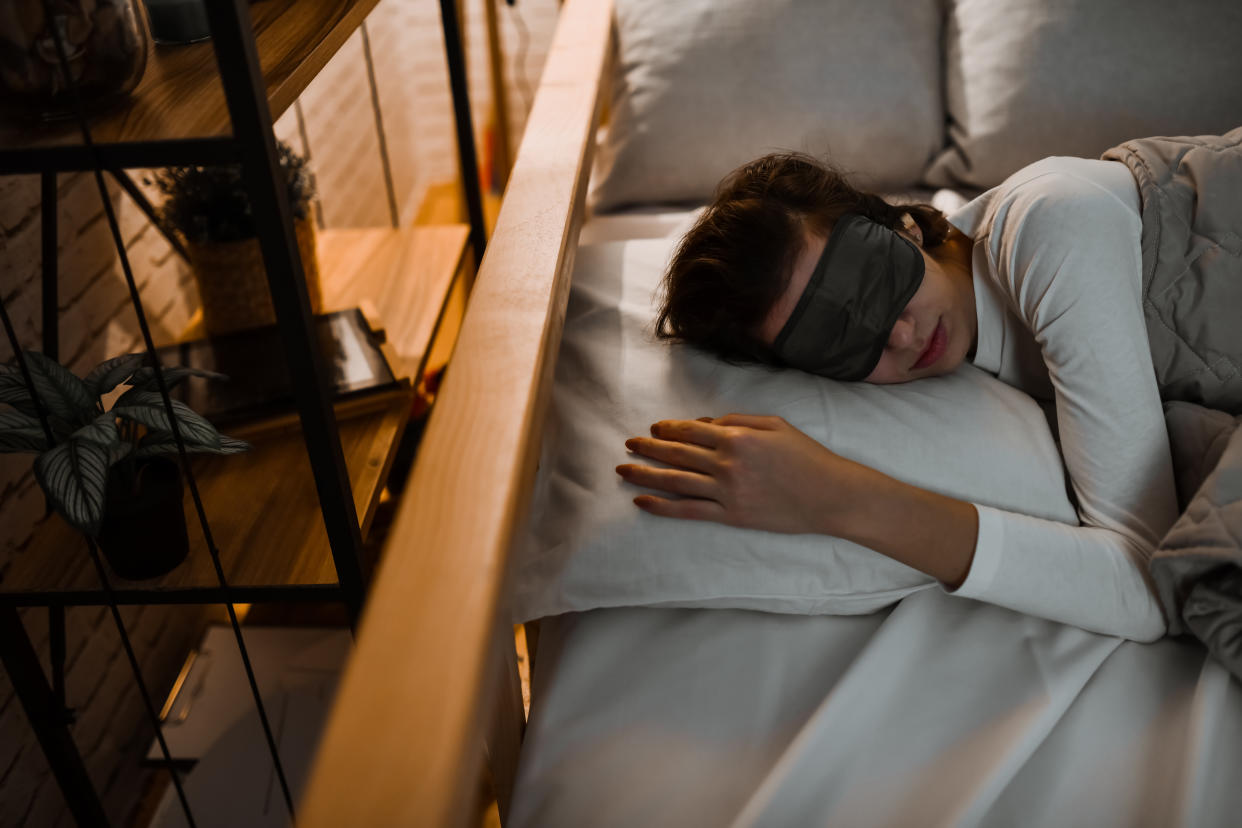 A woman sleeps in a darkened room while wearing a sleep mask