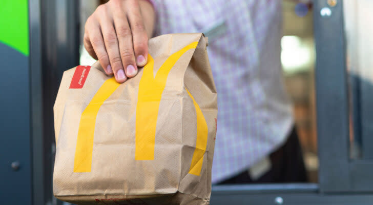 Man holds out a McDonald's bag with the golden arches logo on it at a drive-thru window.