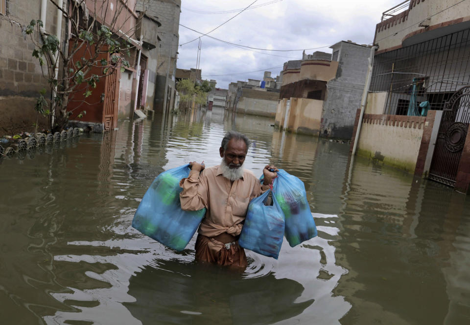 A man carries goods as he wades through flooded street after heavy monsoon rains, in Karachi, Pakistan, Wednesday, Aug. 26, 2020. Pakistan's military said it will deploy rescue helicopters to Karachi to transport some 200 families to safety after canal waters flooded the city amid monsoon rains. (AP Photo/Fareed Khan)