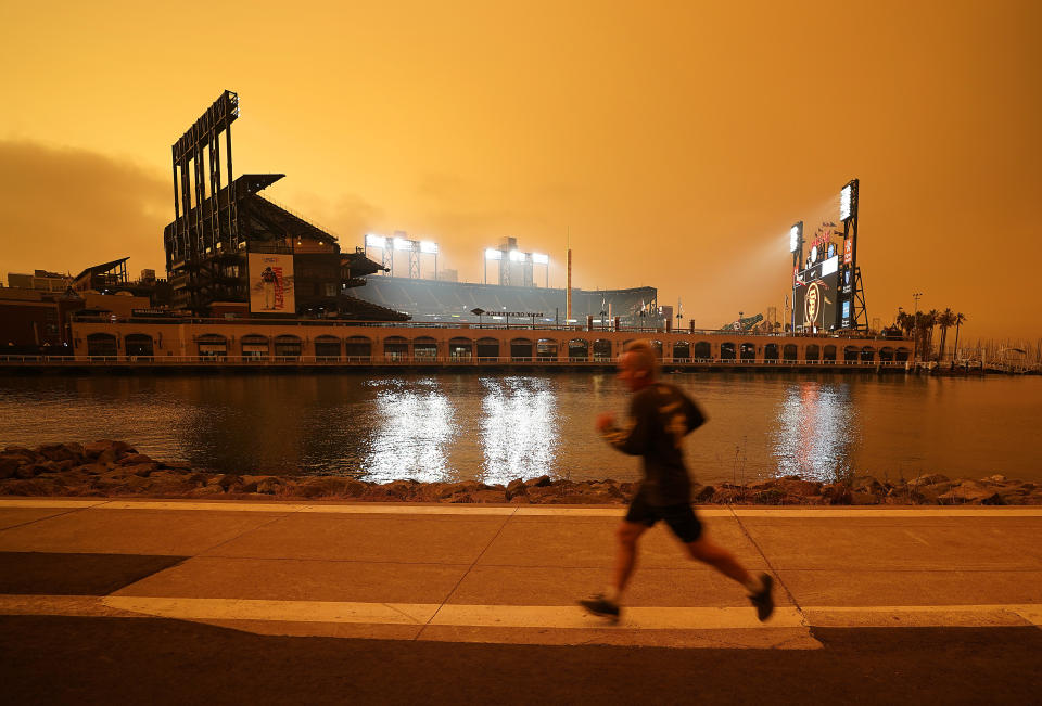 FILE - In this Wednesday, Sept. 9, 2020 file photo, a jogger runs along McCovey Cove outside Oracle Park in San Francisco, under darkened skies from wildfire smoke. Worsening climate change requires that the United States do much more to track and manage flows of migrants fleeing natural disasters. That's the finding of a multiagency study from the Biden administration. President Joe Biden ordered the assessment. (AP Photo/Tony Avelar)