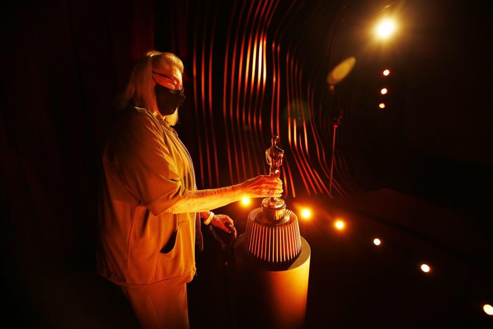 A woman holds an Oscar statuette in a darkened room.