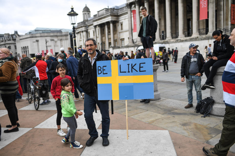 A man holds up a sign urging the UK to implement less restrictions like Sweden.