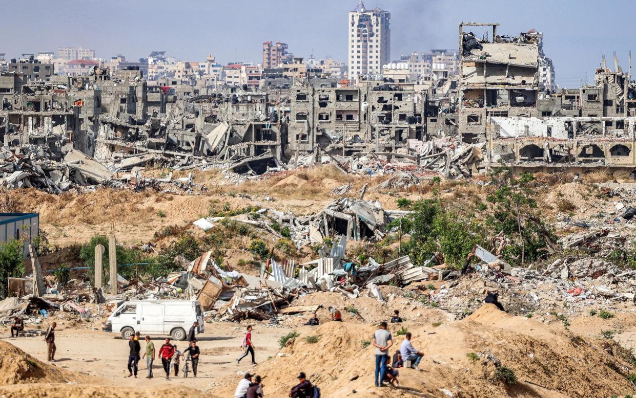 People wait before destroyed buildings in cleared area by the coastline for humanitarian aid packages to drop over the northern Gaza Strip