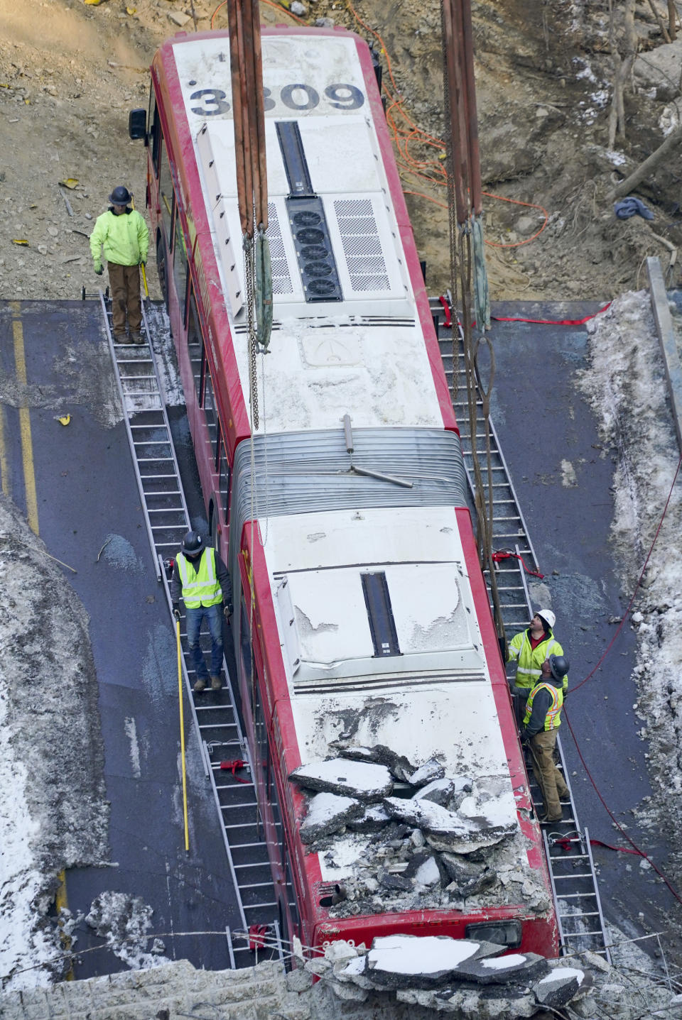 Workers use ladders placed along the sides of the bus that was on a bridge when it collapsed Friday as they work to remove it during the recovery process on Monday Jan. 31, 2022 in Pittsburgh's East End. (AP Photo/Gene J. Puskar)