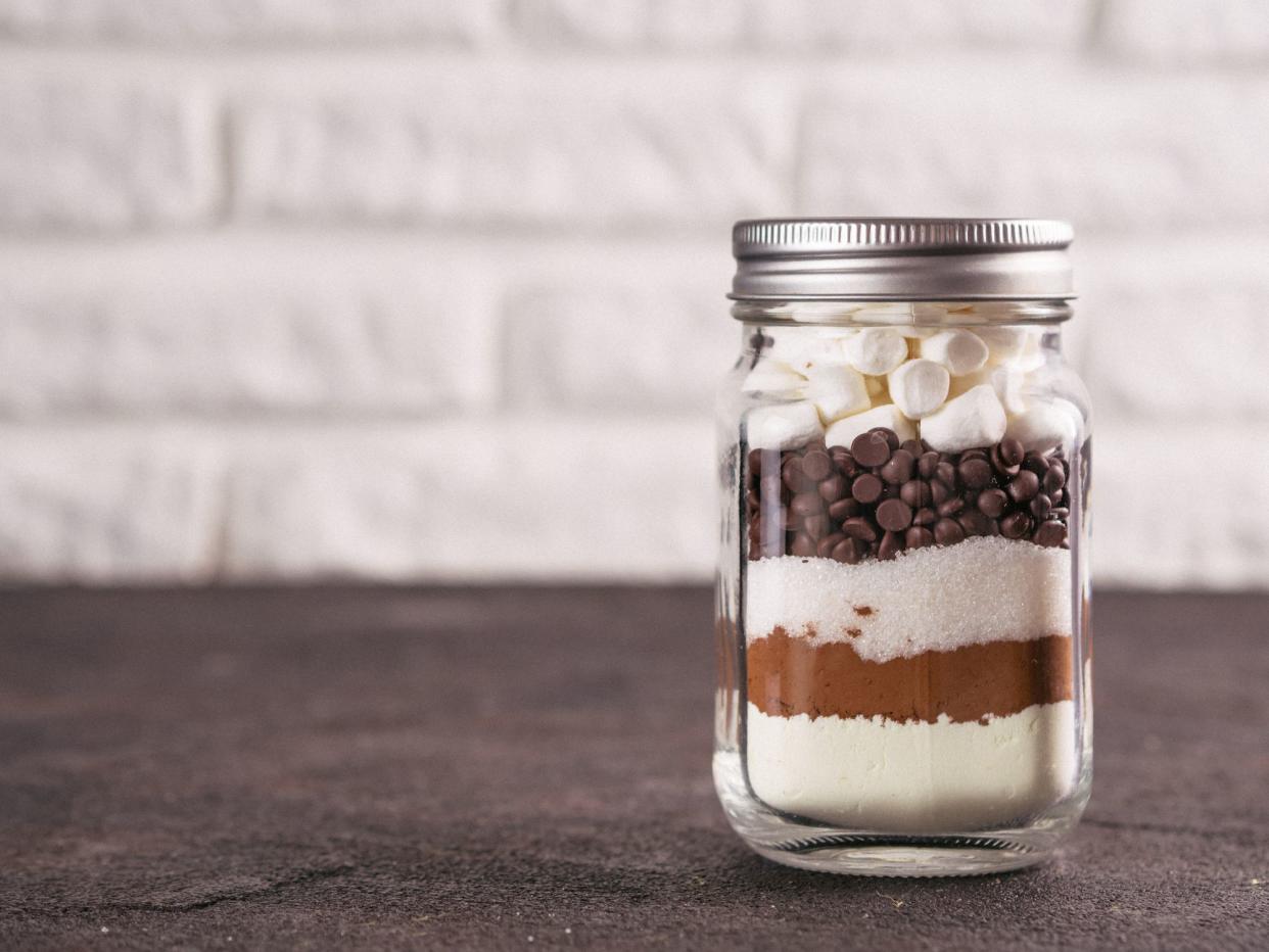 Hot chocolate mix in mason jar. Homemade mix from cocoa, dry milk, sugar, chocolate chips and marshmallows. Christmas and winter holiday budget-friendly holiday gifts idea. Copy space