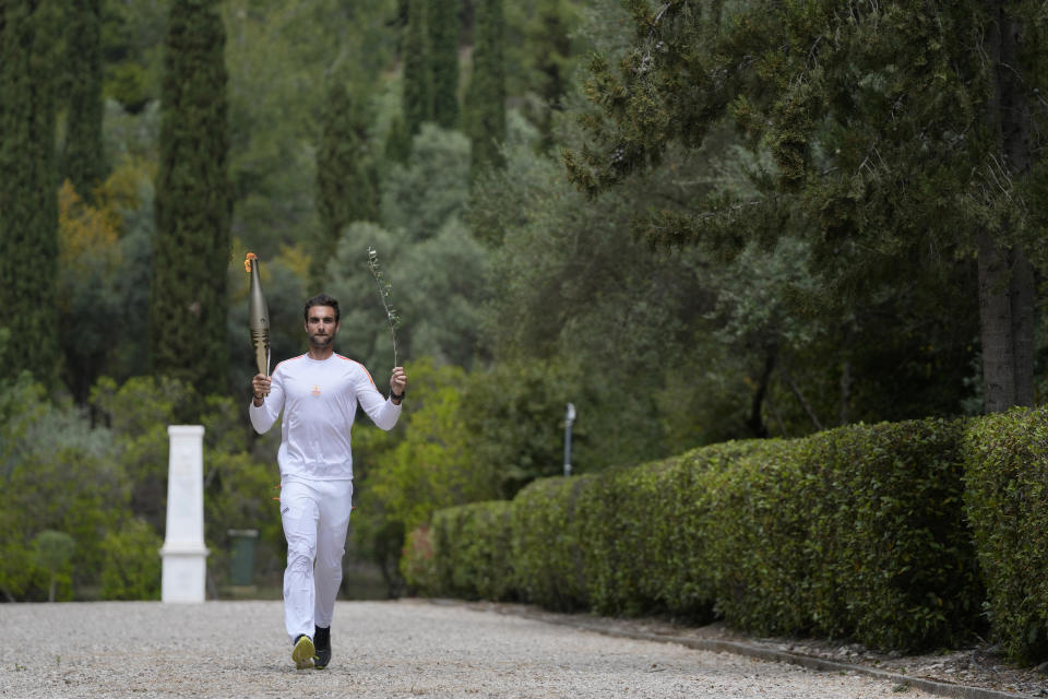 The first torch bearer, Greek olympic gold medalist Stefanos Douskos, returns from the monument to Pierre de Coubertin, in the background, after the official ceremony of the flame lighting for the Paris Olympics, at the Ancient Olympia site, Greece, Tuesday, April 16, 2024. The flame will be carried through Greece for 11 days before being handed over to Paris organizers on April 26. (AP Photo/Thanassis Stavrakis)