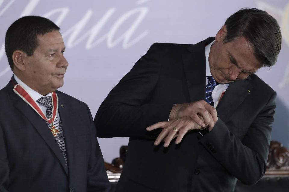 Brazil's President Jair Bolsonaro, right, looks at his watch standing next to Vice President Hamilton Mourao, during a decoration ceremony of the Maua Merit Medal, in Brasilia, Brazil, Thursday, Aug. 15, 2019. Norway suspended funding to Brazil’s Amazon Fund, created to fight deforestation in the country’s vast rainforest, a spokesperson for the Norwegian environment ministry said Thursday. The decision blocks the transfer of 300 million Krones (over $44 million) in financial aid to local projects in the Amazon, the ministry confirmed. (AP Photo/Eraldo Peres)