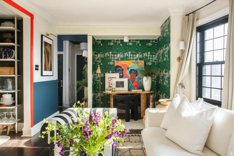 A brightly colored room with fresh purple flowers, a stripped couch, green and white wallpaper and orange and blue color accents on the walls.