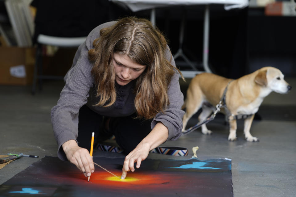 Freyja Ferragamo, 21, with her dog Oliver, who traveled from Arizona with members of the Apache Stronghold, paints a protest banner at Self Help Graphics & Art in the Los Angeles neighborhood of Boyle Heights on Monday, March 20, 2023. The Apache group battling a foreign mining firm that wants to build one of the largest copper mines in the United States on what tribal members say is sacred land will get a new chance to make its point Tuesday when a full federal appeals court panel takes another look at the case. (AP Photo/Damian Dovarganes)