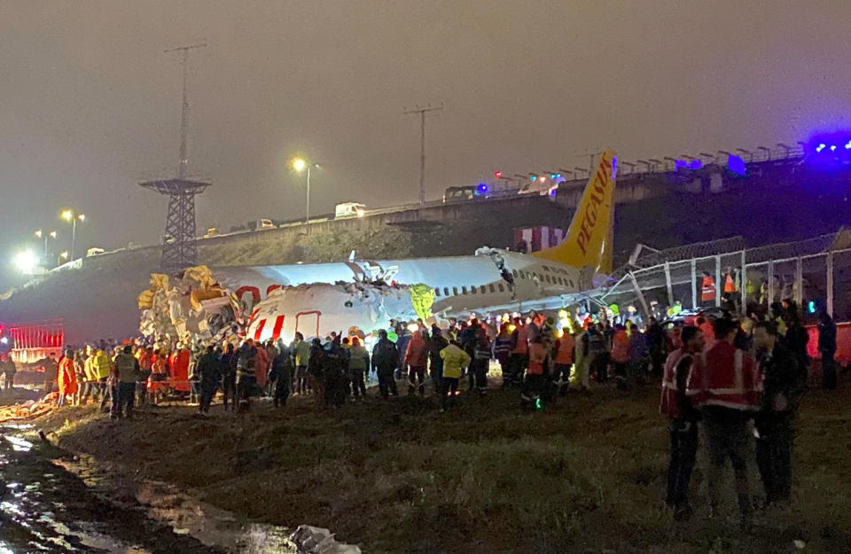 Rescue members and firefighters work after a plane skidded off the runway at Istanbul's Sabiha Gokcen Airport, Istanbul, Wednesday, Feb. 5, 2020. A plane skidded off the runway Wednesday at Istanbul’s Sabiha Gokcen Airport, crashing into a field and breaking into pieces. Passengers were seen evacuating through cracks in the plane and authorities said at least 21 people were injured. (DHA via AP)