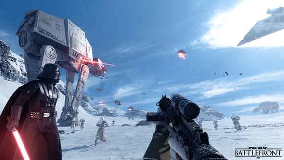 A character holding a gun from the first-person perspective looking at Darth Vader and an AT-AT walker in EA's game Star Wars Battlefront II.