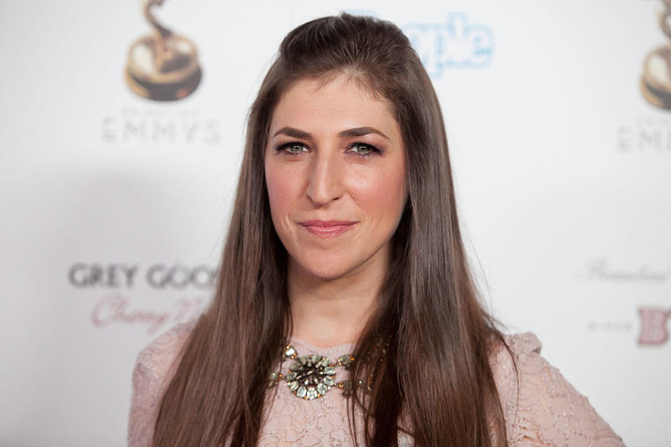 Mayim Bialik smiling at an event, wearing a lace dress with a decorative necklace
