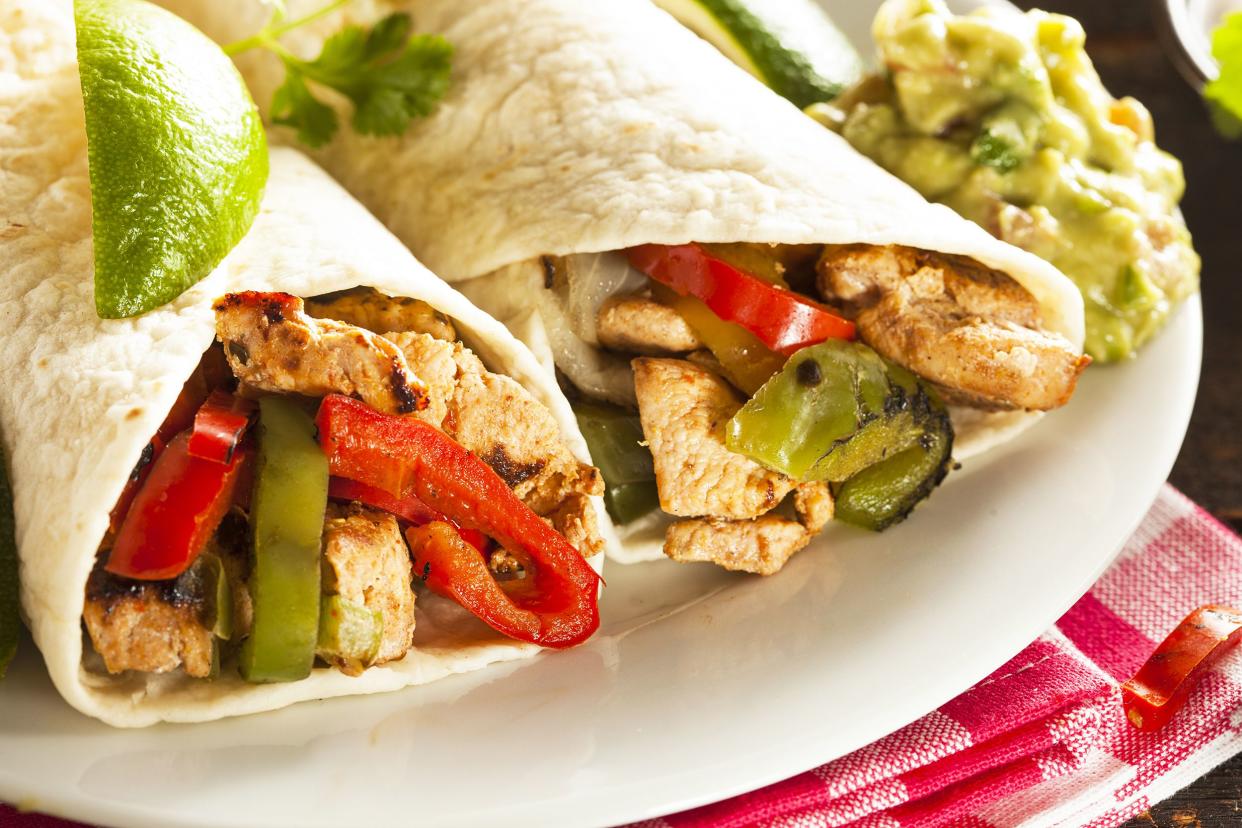 Closeup of chipotle chicken fajitas on a white plate with a slice of lime and guacamole with a red checkered napkin