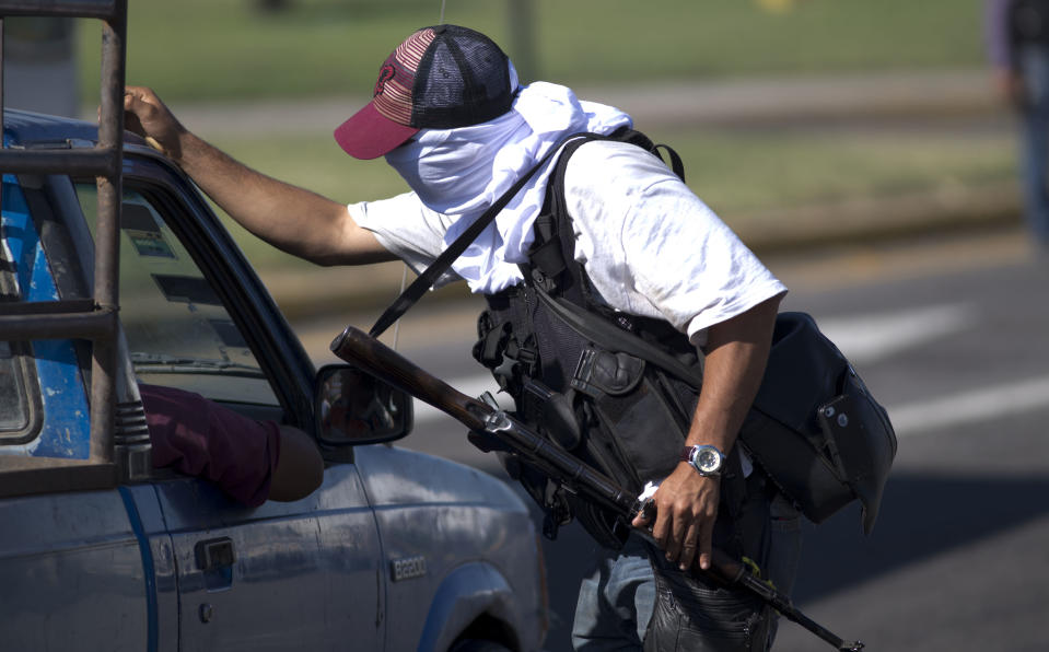 A man belonging to the Self-Defense Council of Michoacan, (CAM), questions the passengers of a vehicle at a checkpoint in the entrance of Nueva Italia, Mexico, Monday, Jan. 13, 2014. A day earlier the self-defenses encountered resistance as they tried to rid the town of the Knights Templar drug cartel while the government announced today that federal forces will take over security in a large swath of a western Mexico that has been hard hit by violence. (AP Photo/Eduardo Verdugo)