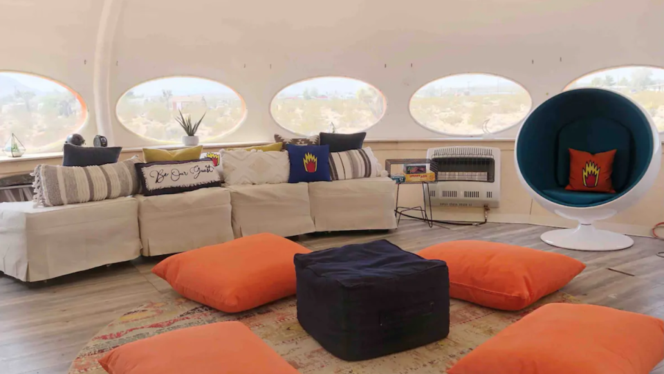 The interior of the Area 55 Futuro House, featuring a couch, bean bags and pillows, and pod-like chairs.