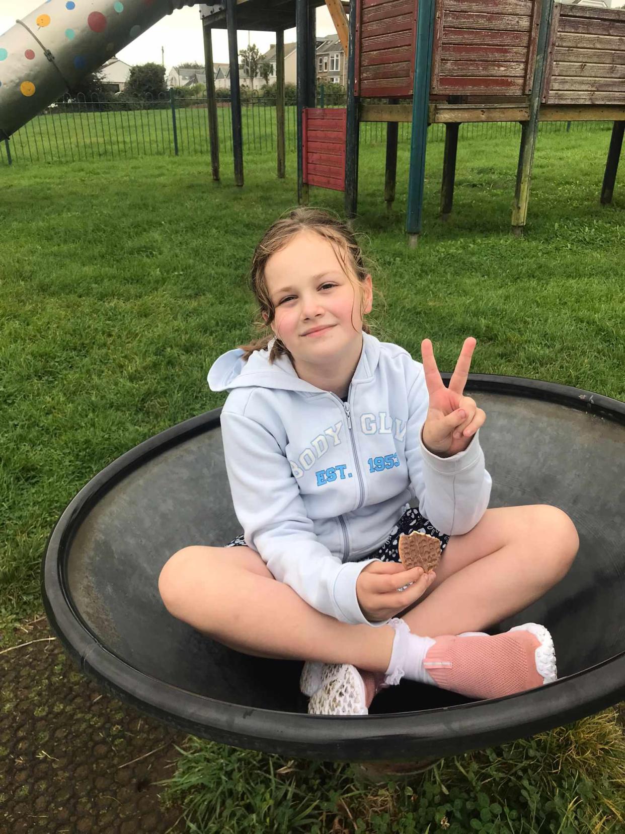 Girl sits cross-legged on a black apparatus while giving the peace sign