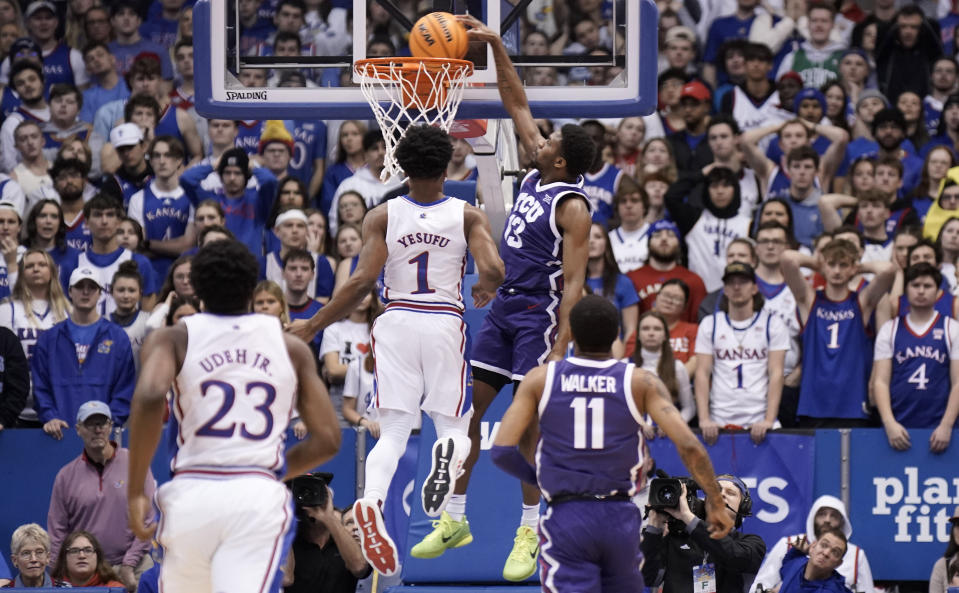 TCU guard Shahada Wells (13) comes in for a dunk past Kansas guard Joseph Yesufu (1) during the first half of an NCAA college basketball game on Saturday, Jan. 21, 2023, at Allen Fieldhouse in Lawrence, Kan. TCU defeated Kansas, 83-60. (AP Photo/Nick Krug)