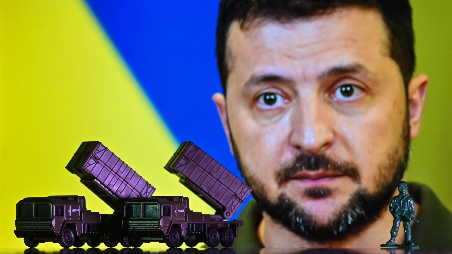  Illustration of a mini replica of MIM-104 Patriot, a surface-to-air missile (SAM) system, seen in front of a photo of Volodymyr Zelenskiy. 