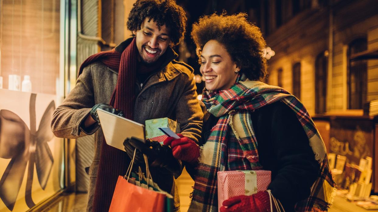 Smiling young couple buying Christmas presents online using a credit card and a digital tablet.