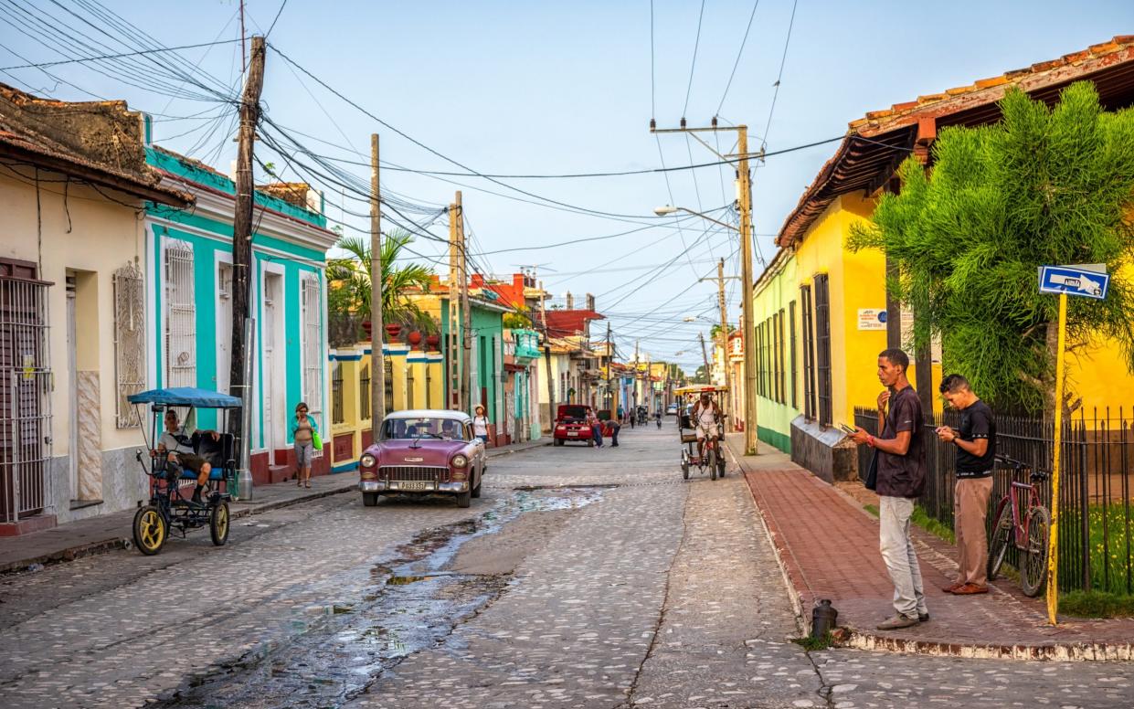 Locals, bike taxi and Vintage car near colonial houses in the old town of Trinidad, Cuba