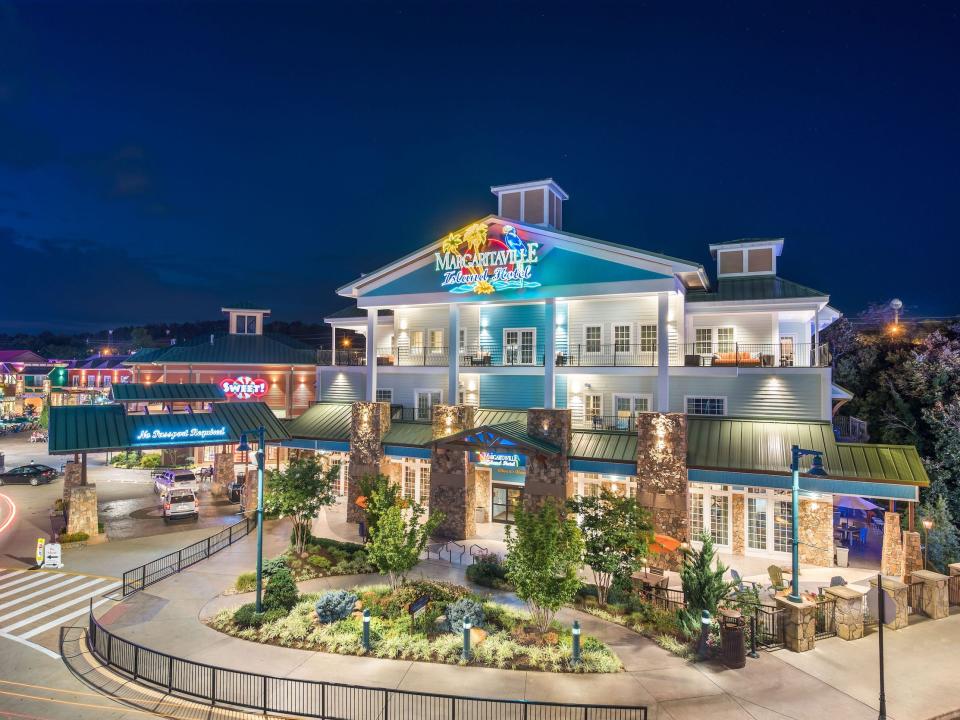 A Margaritaville hotel at night among other glowing stores