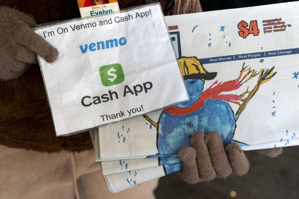 A vendor selling Street Sense, a local paper that covers issues related to the homeless and employs unhoused individuals as its vendors, holds up her sign saying she can accept donations from cashless apps like Venmo and CashApp, Wednesday, Dec. 6, 2023, in Washington. The transition to a cashless society has impacted street-level charitable giving – from individual donations to panhandlers to the Salvation Army donation kettles. (AP Photo/Jacquelyn Martin)