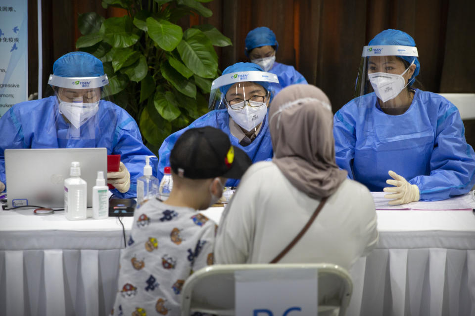 Workers wearing protective gear register a person during a COVID-19 vaccination session for resident foreign journalists at a vaccination center in Beijing, Tuesday, March 23, 2021. Chinese medical firm Sinovac said its COVID-19 vaccine is safe in children ages 3-17, based on preliminary data, and it has submitted the data to Chinese drug regulators. State-owned Sinopharm, who has two COVID-19 vaccines, is also investigating the effectiveness of its vaccines in children. (AP Photo/Mark Schiefelbein)