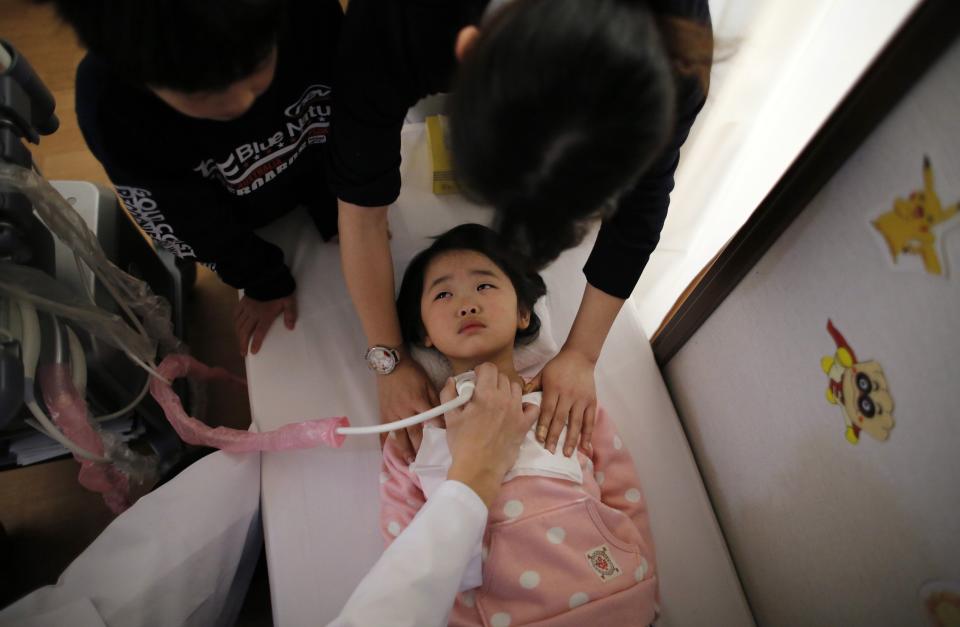 A doctor conducts a thyroid examination on five-year-old girl as her older brother and a nurse take care of her at a clinic in temporary housing complex in Nihonmatsu, west of the tsunami-crippled Fukushima Daiichi nuclear power plant, Fukushima prefecture February 27, 2014. (REUTERS/Toru Hanai)