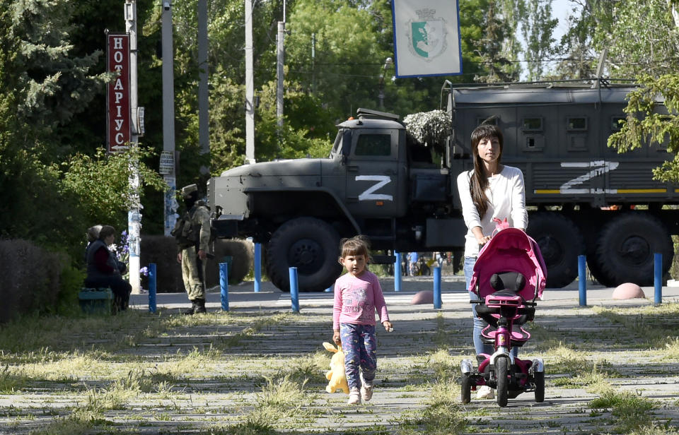 This photo taken on May 20, 2022 shows a womand and child walking in a park as Russian servicemen patrol  the street in Skadovsk, Kherson Oblast, amid the ongoing Russian military action in Ukraine.