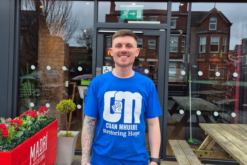 Gareth Madden outside his workplace, The Burger Club in Belfast, wearing a Cuan Mhuire t-shirt